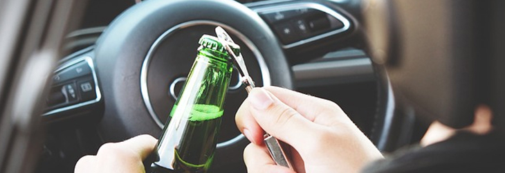 A picture of a guy opening a beer in the car